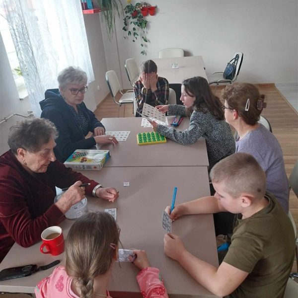 Przy stole siedzą osoby dorosłe i dzieci, grają razem w gry.